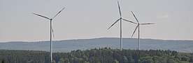 Drei Windräder in einer hügeligen Landschaft.